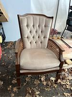 Front view of wooden armchair with tufted beige upholstery and caned arms.