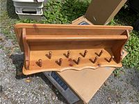 View of the front side of the wooden hanging shelf showing ten rounded pegs and scalloped edge detail.