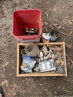 Wooden box and red bucket containing various old metal hardware pieces and porcelain knobs.