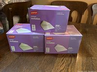 Three boxes of Staples invitation envelopes on wood table; two boxes unopened, one with some missing envelopes.