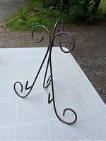 Front view of dark metal mini display stand on white table, showing curled support loops