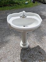 Front view of white ceramic pedestal sink with chrome faucet installed on top, showing overall shape and condition.
