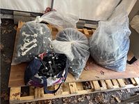 Four bags filled with plastic hangers, mostly black with some white/cream, on wooden pallets.