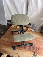 Front view of the reverse desk chair showing cushioned seat and knee rest with geometric upholstery pattern and caster wheels.