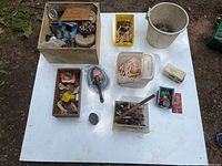 Top-down view of all containers and bins with varied hardware items spread on a white surface outdoors