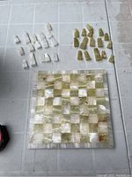 16 white and 16 light green carved stone chess playing pieces arranged around board