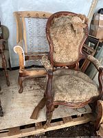Wing chair with worn upholstery and wooden frame showing damage and exposed stuffing.