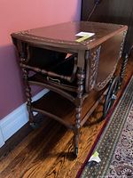 Side view of oak tea wagon showing drop leaf sides, turned legs, lower shelf and castor wheels