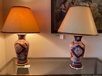 Both Imari-style lamps displayed side by side on glass console table under artwork