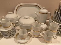 Full display of plates, cups, pots and bowls arranged on table showing shapes and gold trim.