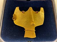 Front view of abstract face brooch in navy velvet box