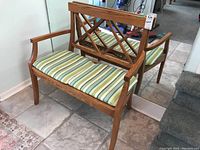 Front view of wooden bench with crisscross backrest and striped cushioned seat two cushions side by side.