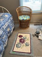 Photo showing the rattan chair with blue and yellow floral cushion beside a bed, and the floral floor mat placed in front of the chair on light carpet floor.