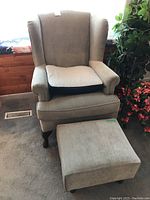 Front view of beige upholstered wingback chair with gel pad cushion on the seat and matching ottoman in front.