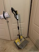 Full view of the electric snow shovel standing upright, showing handle and shovel base.