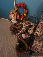 Photo showing multiple faux flower arrangements in cream, pink, and purple tones, several woven baskets, two wreaths, and a woven straw hat with ribbon and decorative flowers.