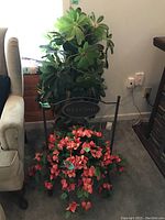 Wide view showing faux green plant in wicker basket and faux pink floral arrangement on black metal Welcome stand near armchair.