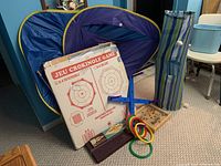 Collection of boxed and loose board games and game accessories including Crokinole, Cribbage boards, ring toss, and a collapsible game enclosure.