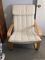 Front view of the wooden IKEA chair with off-white cushioned seat and backrest against a wall.