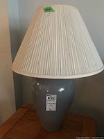 Pair of large ceramic table lamps with off-white fabric shades shown individually on wooden tables.