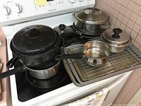 Overhead photo showing black enamel pots stacked on stove, stainless steel saucepan with lid, multiple baking sheets and wire racks arranged on stove top