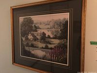 Photo of first framed print showing a countryside cottage by a pond with flowers and trees