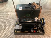 Front and side view of the Imperial Sewing Machine Model B mounted on its base with attached foot pedal and thread spool. Portable carrying case visible in background.