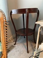 Full view of the two tier wooden side table showing round top and lower shelf with curved legs near a window.