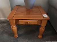 Photo of one wood side table showing the top panel design, drawer with round wooden knob, turned legs, and minor surface marks.