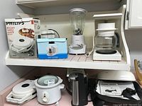 Photo showing all eight appliances on shelves and counter, including waffle maker in box on top shelf, mini chopper in box, blender, toaster, slow cooker, can opener, electric skillet, and coffee maker.