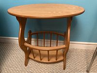 Front view of solid wood oval side table showing integrated magazine holder and curved supports.