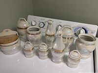 Full view of all 10 ceramic jars with gold etching and printed labels on a white surface