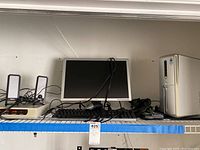 Photo showing Dell PC tower, monitor, keyboard, speakers and mouse placed on a shelf alongside a white Memorex power center and computer parts.