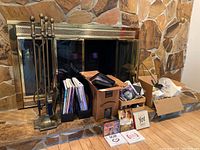 Full view of fireplace tools with stand, magazines or vinyl records, CDs, DVDs, and miscellaneous items arranged on stone hearth in front of fireplace.