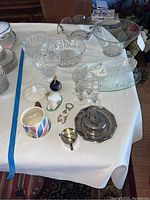 Full view of all items on a white cloth including glass bowls, platters, salt and pepper shakers, metal containers, mug, candy dish