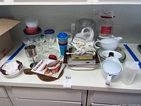 Overview of all kitchenware including plastic containers, dessert glasses, coffee accessories, popcorn popper, Cuisinart cutting board, and miscellaneous items arranged on countertop.