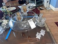 Large heavy glass bowl on wooden table with three sets of glass candle holders, including tall holders with gold-colored candles and smaller clear glass holders.