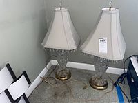 Pair of two matching glass and metal table lamps, each about 28 inches tall with white fabric shades and beaded fringe, shown together from a distance.