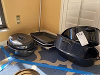 Photo showing several black speckled galvanized metal ovenware items: casserole dishes with lids, rectangular baking trays, and pans, grouped on floor.