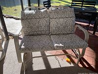 Front view of two-seat rocker glider with patterned seat and back cushions in outdoor setting showing metal frame.