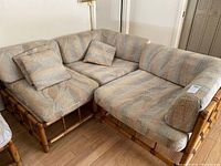 Three pieces of sectional bamboo seats arranged together with cushions on each seat. Worn fabric patterned cushions in neutral colors.