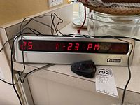 Front view of Telnote digital clock displaying 25 1 23 PM with attached wires and remote control on countertop.