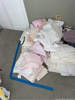 Pile of assorted towels and linens on the floor with white, cream, and pink colors