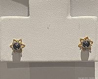 Front view of the pair of 14K gold stud earrings with black pearls set in flower-shaped gold mountings.