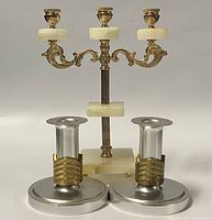 Pair of aluminum candleholders with brass bands in standing position beside marble and brass candelabra.
