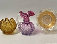 Two vintage glass items displayed together: a cranberry-to-clear blown glass pitcher with melon optic design and a marigold iridescent carnival glass bowl.