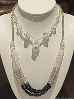 Two beaded crystal necklaces displayed on a white bust stand, showing both necklaces' arrangement and bead details.