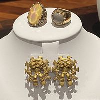 Front view of two rings and pair of gold-tone earrings on white display stand showing stone details and earring design