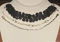 Three bracelets displayed on a neck stand showing two black stone linked bracelets and one delicate silver chain bracelet with small clear stones, all marked 925 silver.