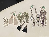 Photo showing six pairs of earrings arranged in a row, with variety of designs and stones, against a light surface.